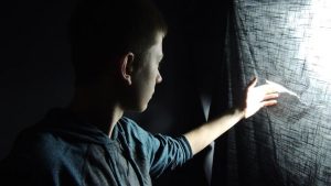 boy looking through a tear in a makeshift curtain
