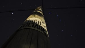 High voltage sign on a pole in the dark - imagery for "Something About Bursting" by Lauren Suchenski